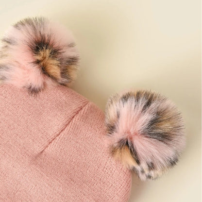 un bonnet rose tout doux avec deux pompons colorés. Sur le revers sont brodés des moustaches, une bouche et une truffe de chat. 