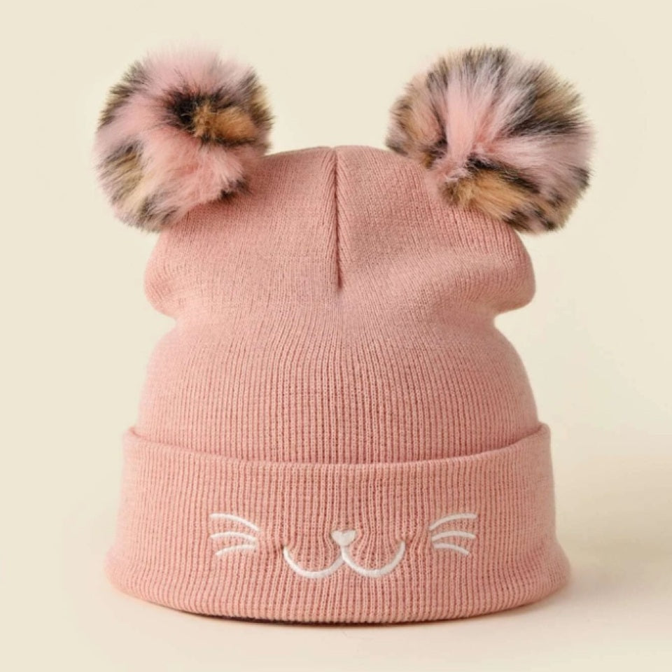 un bonnet rose tout doux avec deux pompons colorés. Sur le revers sont brodés des moustaches, une bouche et une truffe de chat. 