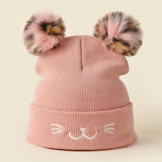 un bonnet rose tout doux avec deux pompons colorés. Sur le revers sont brodés des moustaches, une bouche et une truffe de chat. 