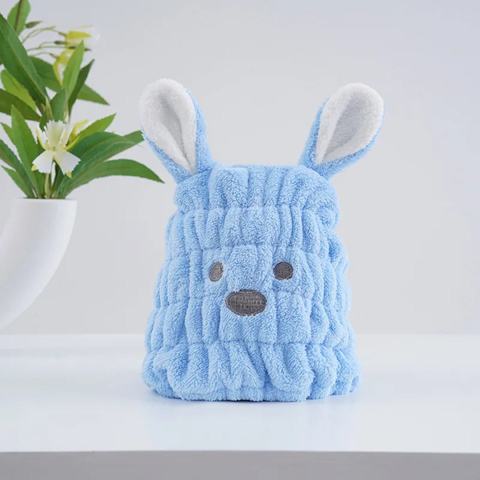 Un bonnet serviette pour cheveux kawaii bleu pastel en forme de petit chien avec deux grandes oreilles, une bouille brodée et une texture douce et moelleuse. Un accessoire pratique et adorable pour un moment cocooning.