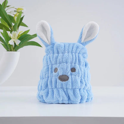 Un bonnet serviette pour cheveux kawaii bleu pastel en forme de petit chien avec deux grandes oreilles, une bouille brodée et une texture douce et moelleuse. Un accessoire pratique et adorable pour un moment cocooning.