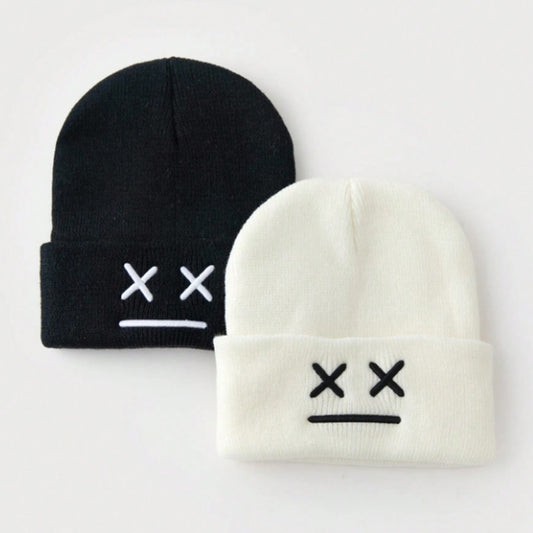 un bonnet à revers noir ou blanc brodé, représentant des yeux en forme de croix et une bouche minimaliste. Design tendance, moderne et minimaliste pour un look urbain street wear adorable.
