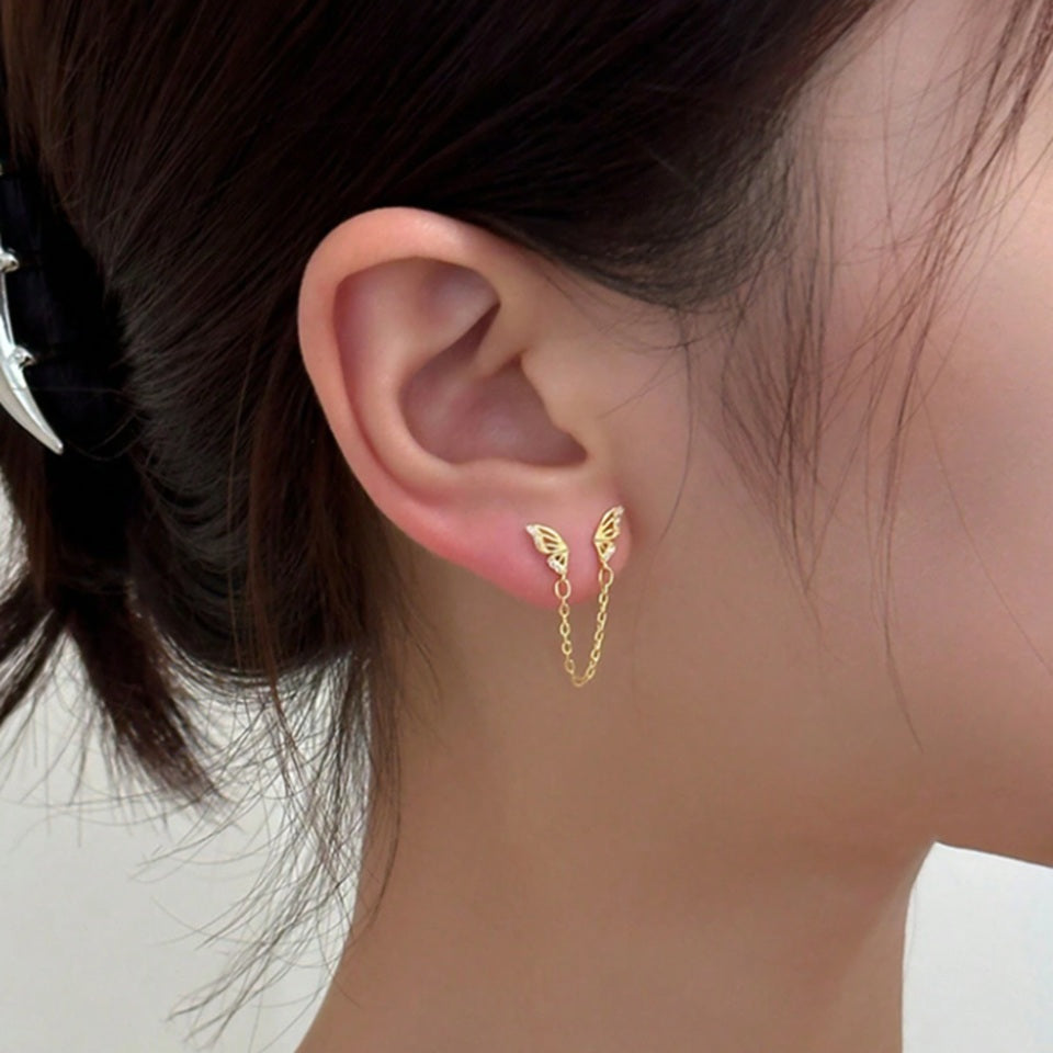 une boucle d'oreilles doré composée de deux papillons dorés tout en strass reliés par une chainette.