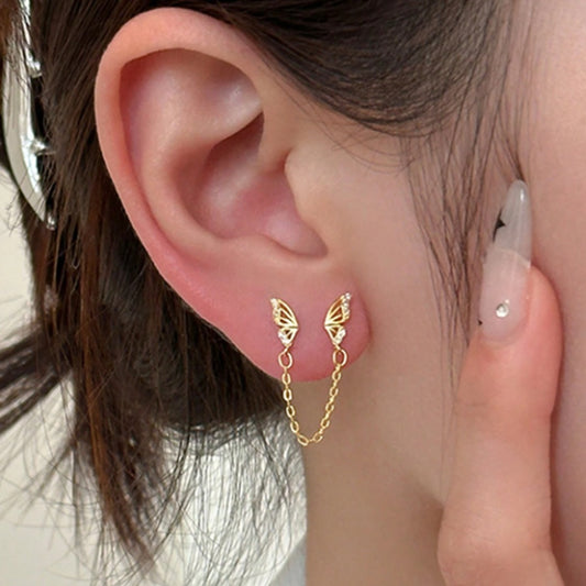 une boucle d'oreilles doré composée de deux papillons dorés tout en strass reliés par une chainette.