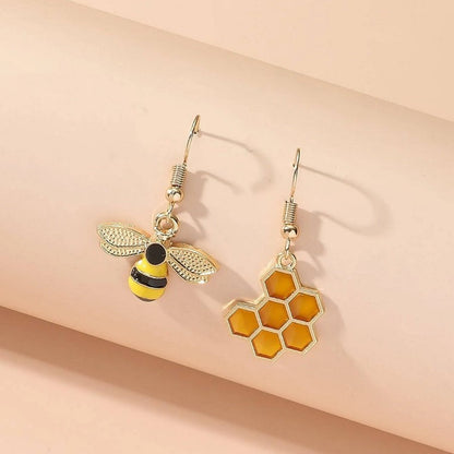 une paire de boucles d'oreilles asymétriques, d'un côté une abeille en strass et de l'autre un rayon de miel