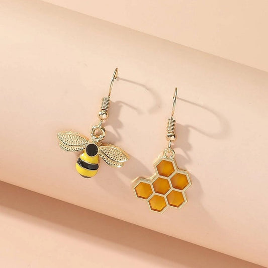 une paire de boucles d'oreilles asymétriques, d'un côté une abeille en strass et de l'autre un rayon de miel