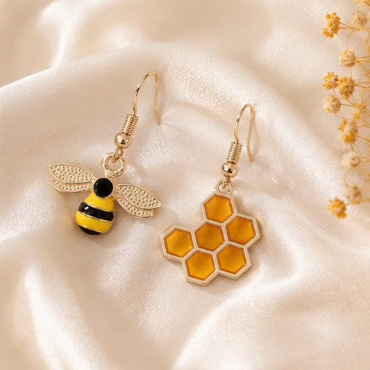 une paire de boucles d'oreilles asymétriques, d'un côté une abeille en strass et de l'autre un rayon de miel