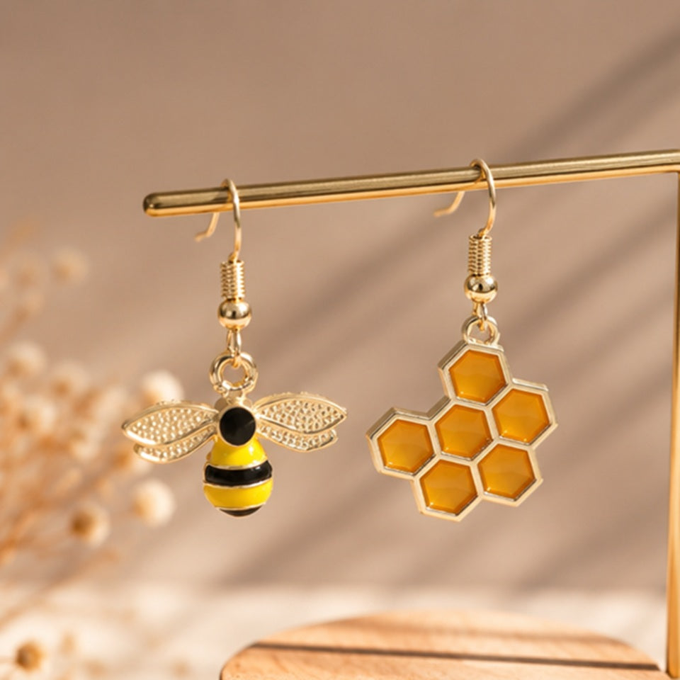 une paire de boucles d'oreilles asymétriques, d'un côté une abeille en strass et de l'autre un rayon de miel