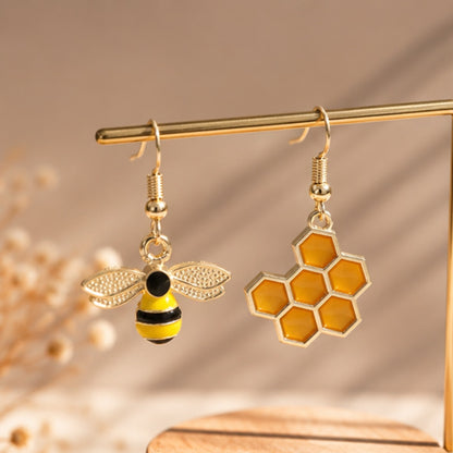 une paire de boucles d'oreilles asymétriques, d'un côté une abeille en strass et de l'autre un rayon de miel