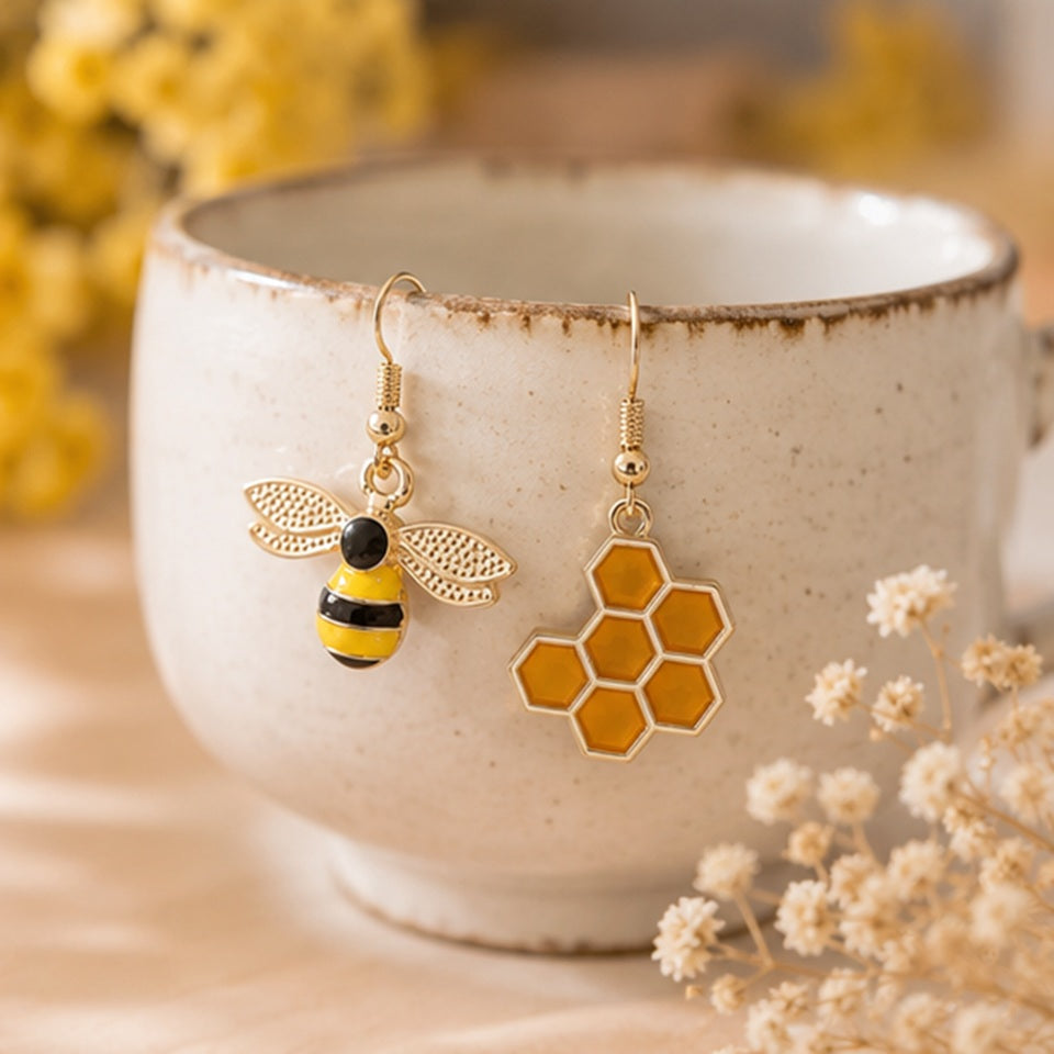 une paire de boucles d'oreilles asymétriques, d'un côté une abeille en strass et de l'autre un rayon de miel