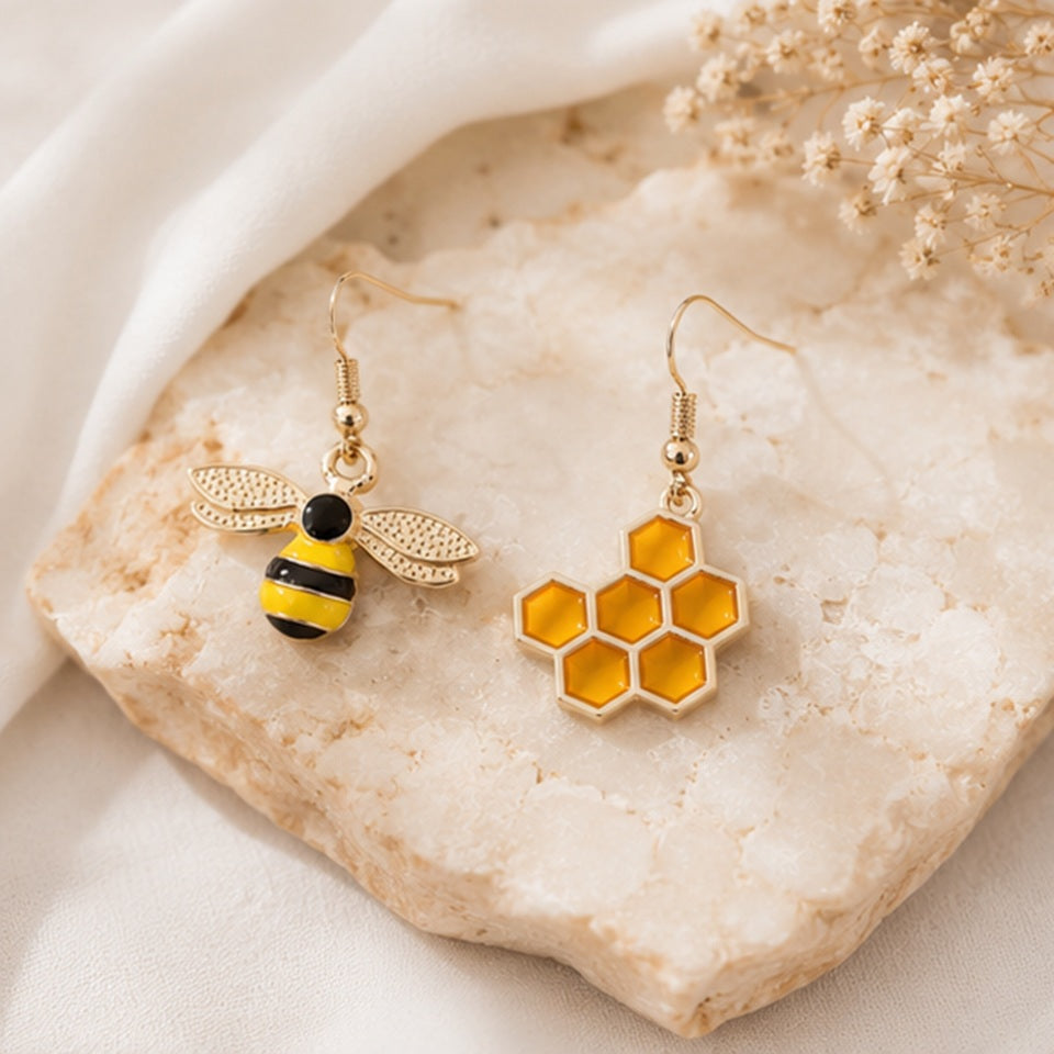 une paire de boucles d'oreilles asymétriques, d'un côté une abeille en strass et de l'autre un rayon de miel