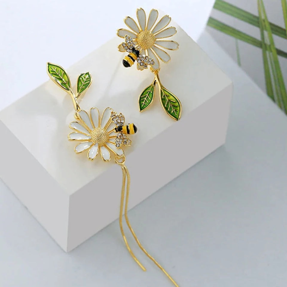 des boucles d'oreilles asymétriques d'une abeille qui butine une fleur et d'une grosse fleur blanche. 
