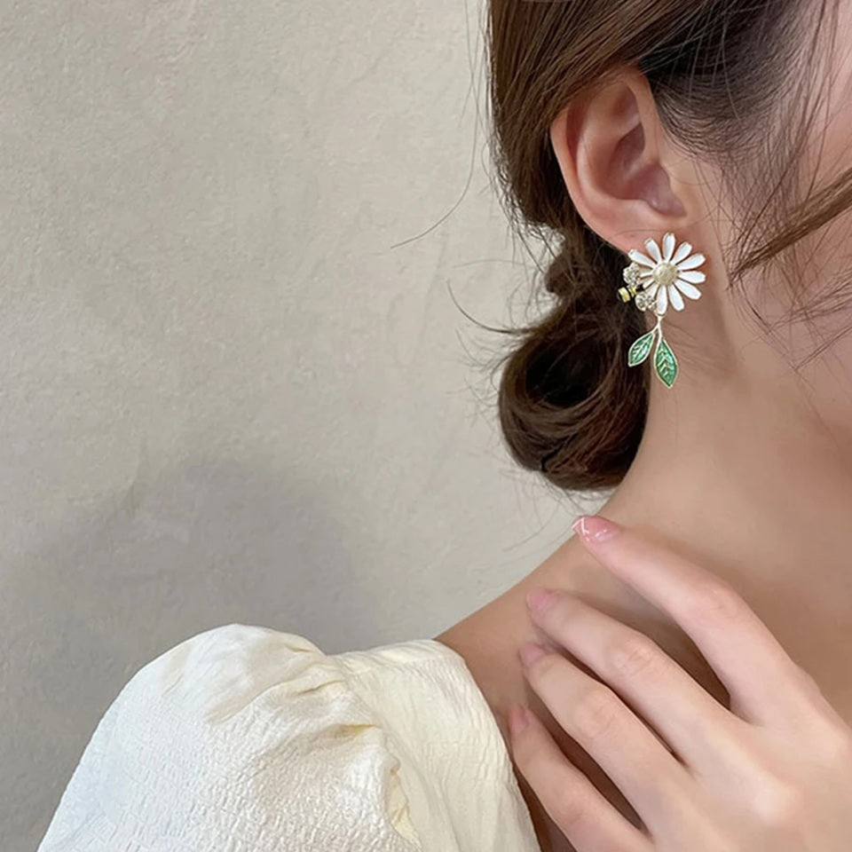 des boucles d'oreilles asymétriques d'une abeille qui butine une fleur et d'une grosse fleur blanche. 