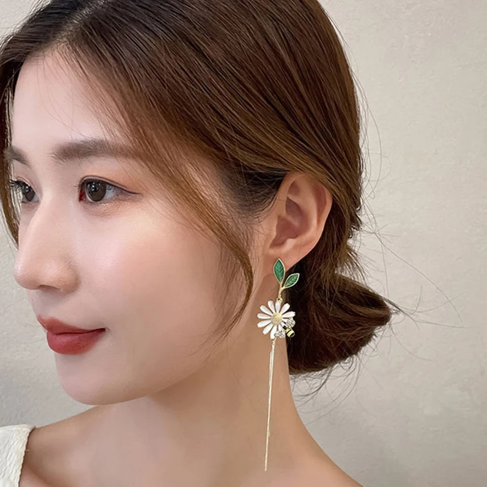 des boucles d'oreilles asymétriques d'une abeille qui butine une fleur et d'une grosse fleur blanche. 
