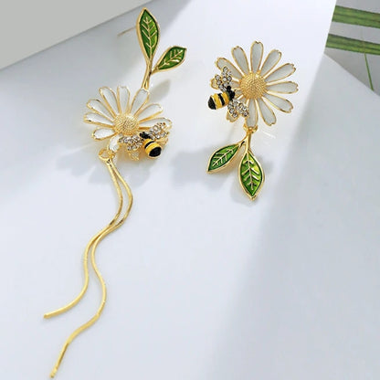 des boucles d'oreilles asymétriques d'une abeille qui butine une fleur et d'une grosse fleur blanche. 