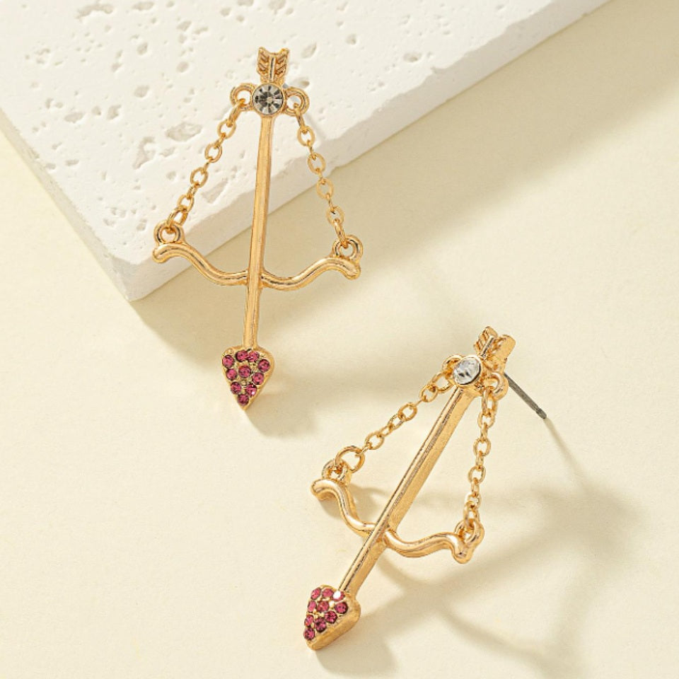 une paire de boucles d'oreilles en forme d'arc de cupidon avec sa flèche à la pointe strass roses