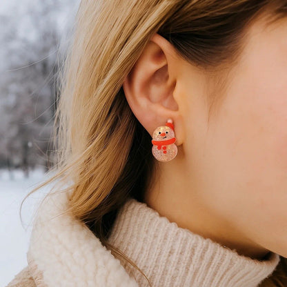 une paire de boucles d'oreilles en forme de bonhomme de neige qui porte un bonnet et une écharpe rouge. Ils sont tous pailletés et rappellent avec tendresse la brillance de l'hiver et de la neige.
