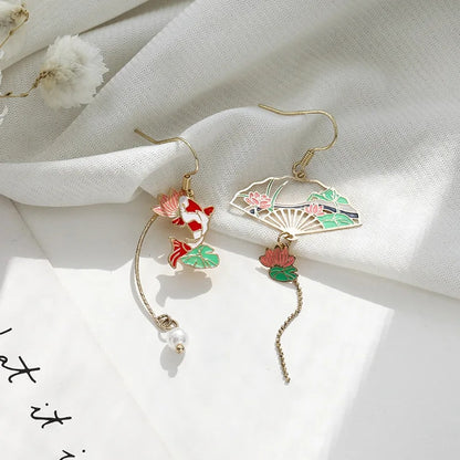 une paire de boucles d'oreilles asymétriques composées d'une carpe koï rouge et blanche et d'une perle ainsi que d'un éventail au motif de nénuphar.