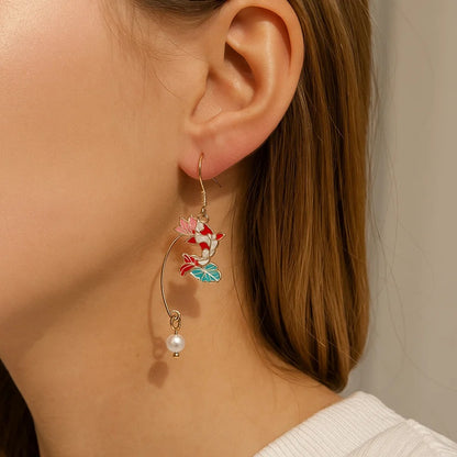 une paire de boucles d'oreilles asymétriques composées d'une carpe koï rouge et blanche et d'une perle ainsi que d'un éventail au motif de nénuphar.