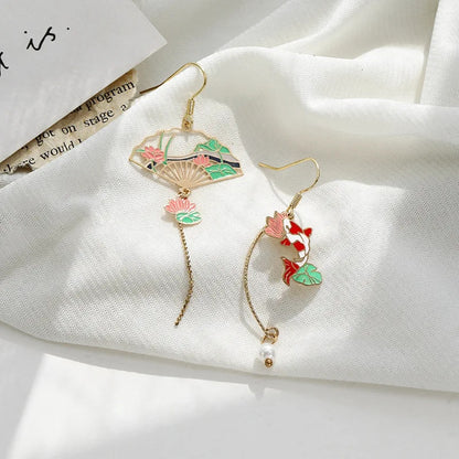 une paire de boucles d'oreilles asymétriques composées d'une carpe koï rouge et blanche et d'une perle ainsi que d'un éventail au motif de nénuphar.
