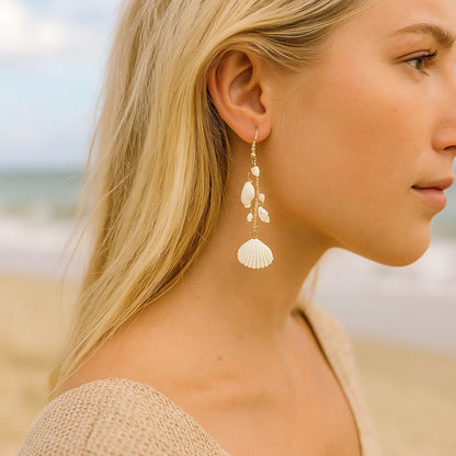 des boucles d'oreilles longues et dorées formées de divers coquillages blancs. L'ensemble évoque les vacances, la plage et l'été.