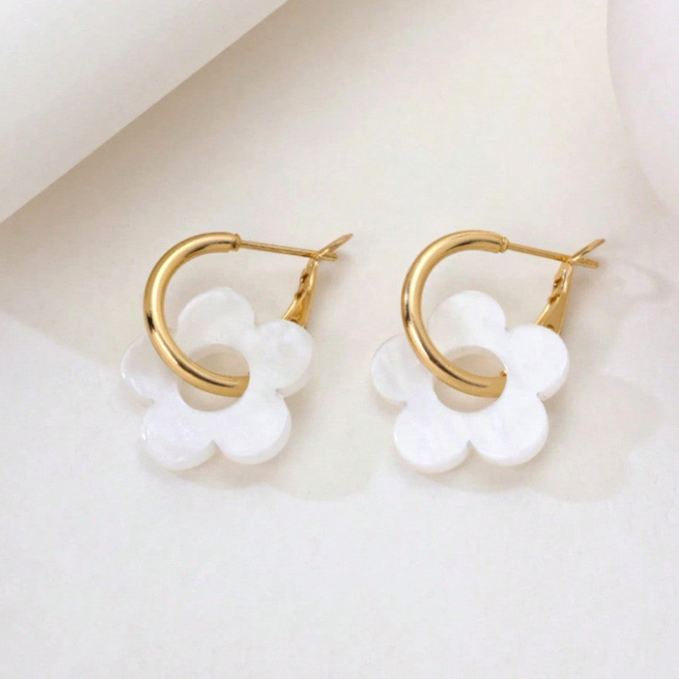 une paire de boucles d'oreilles créoles dorées dans lesquelles se trouve une jolie fleur blanche en acrylique. Style bohème chic