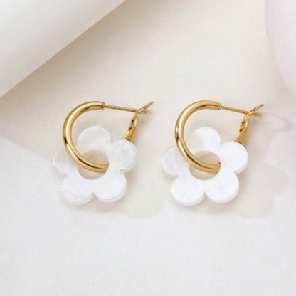 une paire de boucles d'oreilles créoles dorées dans lesquelles se trouve une jolie fleur blanche en acrylique. Style bohème chic