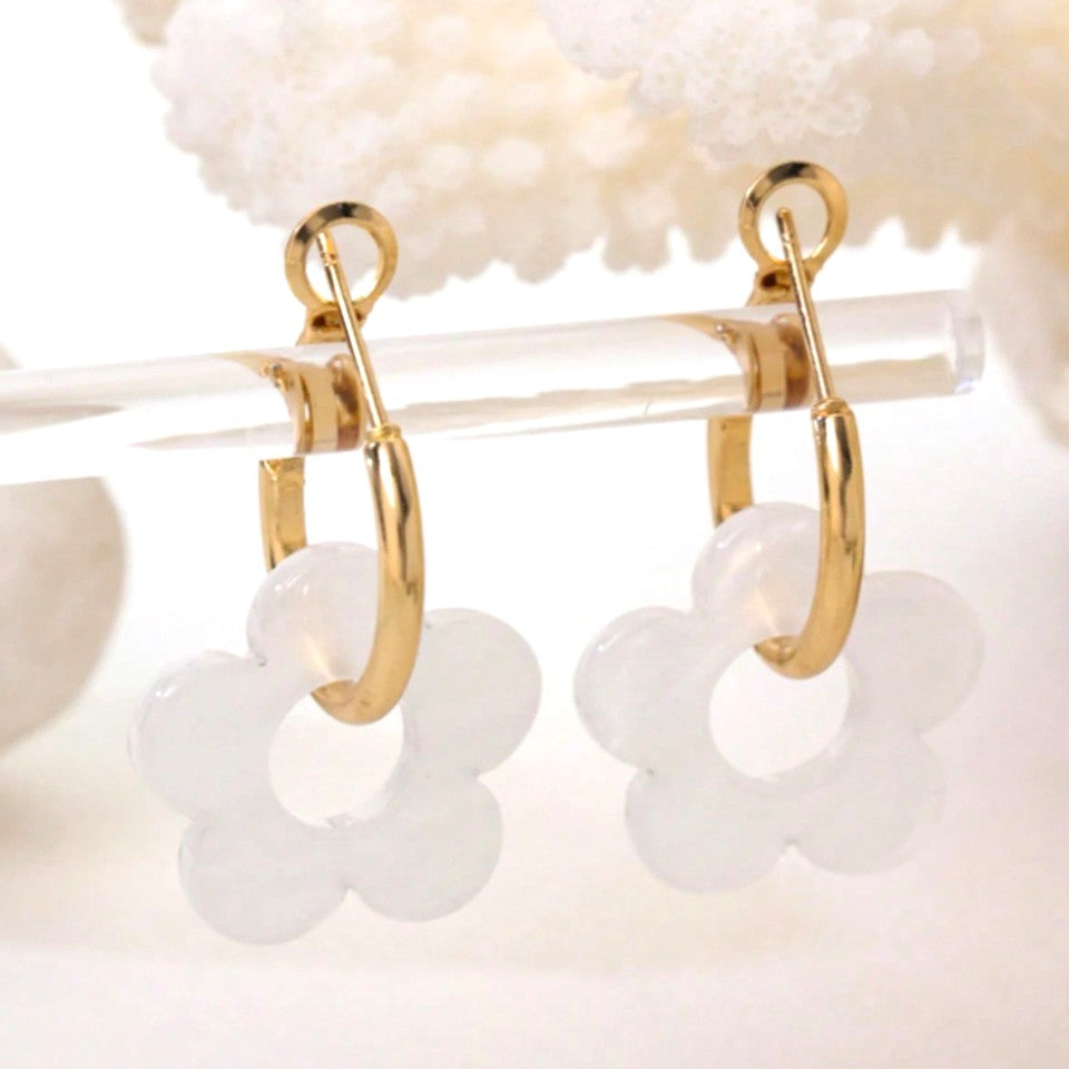 une paire de boucles d'oreilles créoles dorées dans lesquelles se trouve une jolie fleur blanche en acrylique. Style bohème chic