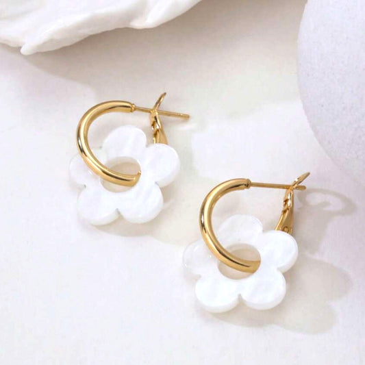 une paire de boucles d'oreilles créoles dorées dans lesquelles se trouve une jolie fleur blanche en acrylique. Style bohème chic