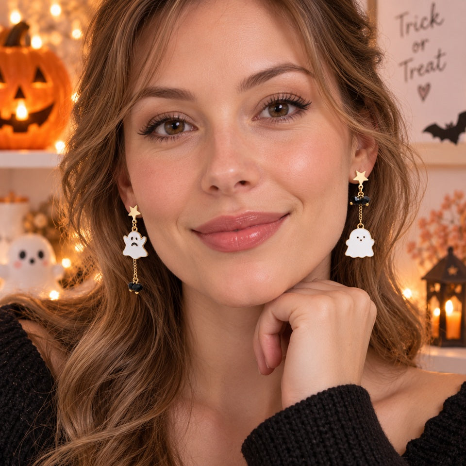 Femme portant des boucles d’oreilles asymétriques fantômes kawaii avec étoiles dorées, chaînes et perles noires, dans une ambiance Halloween chaleureuse.
