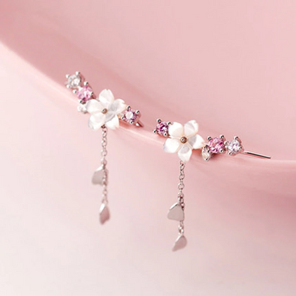 une paire de boucles d'oreilles qui épousent le lobe de l'oreille avec délicatesse et élégance. Une jolie fleur de sakura blanche et des strass blancs et roses viennent embellir l'ensemble. ne petite chaine pendante ornée de pétale de sakura est suspendue aux boucles.