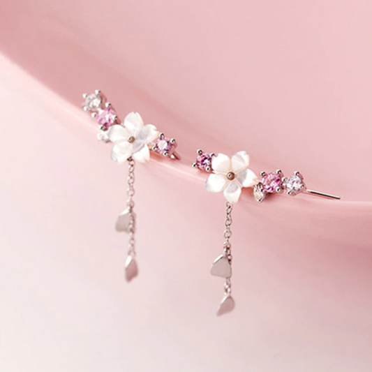 une paire de boucles d'oreilles qui épousent le lobe de l'oreille avec délicatesse et élégance. Une jolie fleur de sakura blanche et des strass blancs et roses viennent embellir l'ensemble. ne petite chaine pendante ornée de pétale de sakura est suspendue aux boucles.