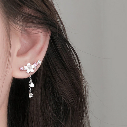 une paire de boucles d'oreilles qui épousent le lobe de l'oreille avec délicatesse et élégance. Une jolie fleur de sakura blanche et des strass blancs et roses viennent embellir l'ensemble. ne petite chaine pendante ornée de pétale de sakura est suspendue aux boucles.