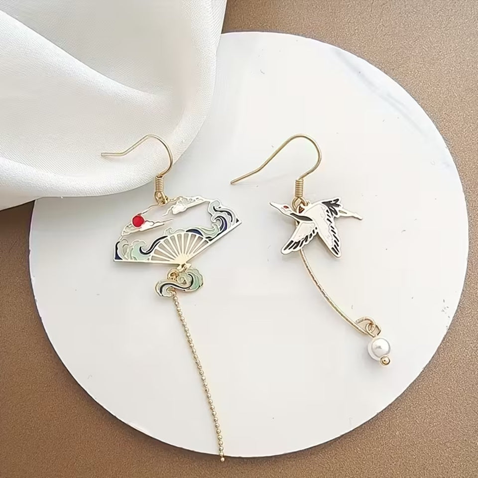 une paire de boucles d'oreilles dorés asymétriques. D'un côté, une grue japonaise et de l'autre, un éventail au motif de la grande vague de Kanagawa. Esthétique qui rappelle les estampes japonaises. Bijou élégant.