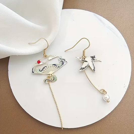 une paire de boucles d'oreilles dorés asymétriques. D'un côté, une grue japonaise et de l'autre, un éventail au motif de la grande vague de Kanagawa. Esthétique qui rappelle les estampes japonaises. Bijou élégant.
