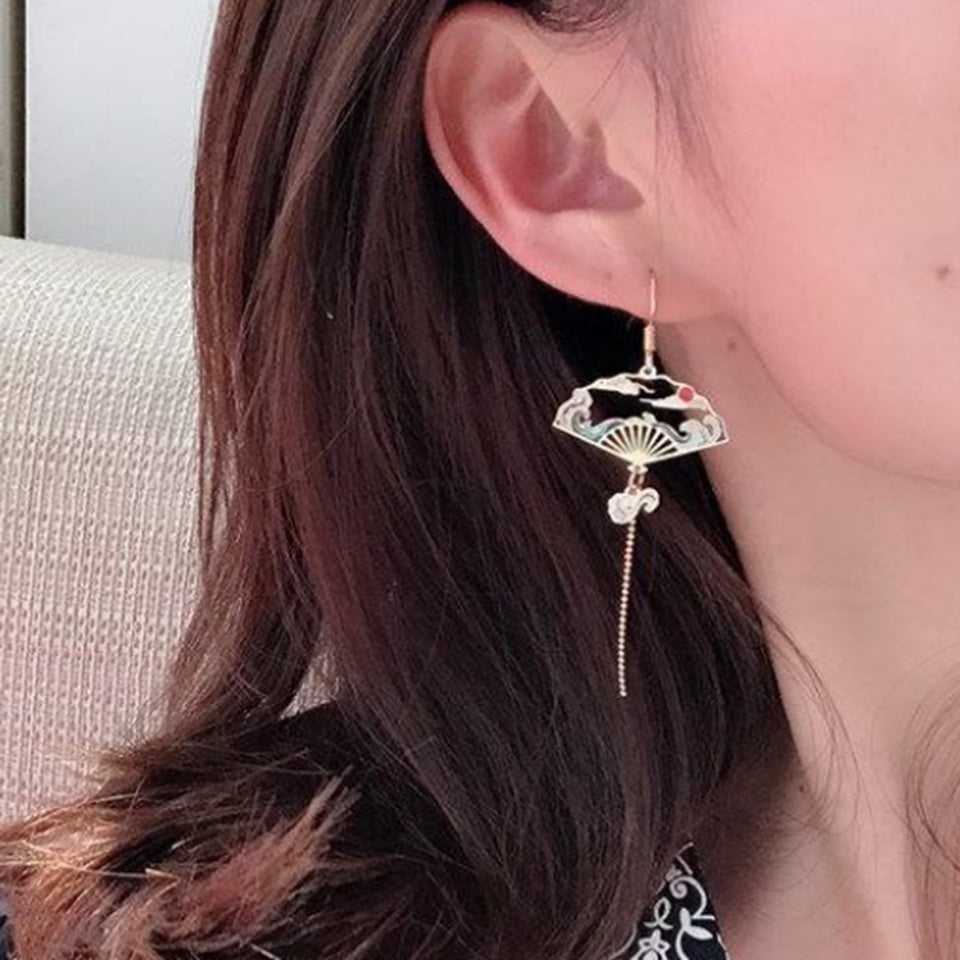 une paire de boucles d'oreilles dorés asymétriques. D'un côté, une grue japonaise et de l'autre, un éventail au motif de la grande vague de Kanagawa. Esthétique qui rappelle les estampes japonaises. Bijou élégant.