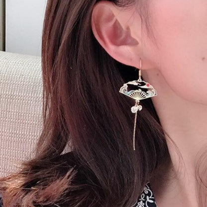 une paire de boucles d'oreilles dorés asymétriques. D'un côté, une grue japonaise et de l'autre, un éventail au motif de la grande vague de Kanagawa. Esthétique qui rappelle les estampes japonaises. Bijou élégant.