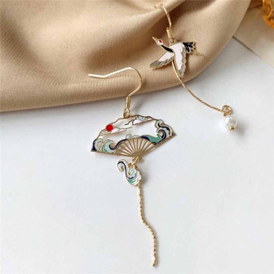 une paire de boucles d'oreilles dorés asymétriques. D'un côté, une grue japonaise et de l'autre, un éventail au motif de la grande vague de Kanagawa. Esthétique qui rappelle les estampes japonaises. Bijou élégant.