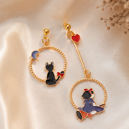 une paire de boucles d'oreilles asymétriques inspirées de Kiki la petite sorcière. D'un côté il y a Jiji le chat noir et de l'autre, Kiki sur son balai.