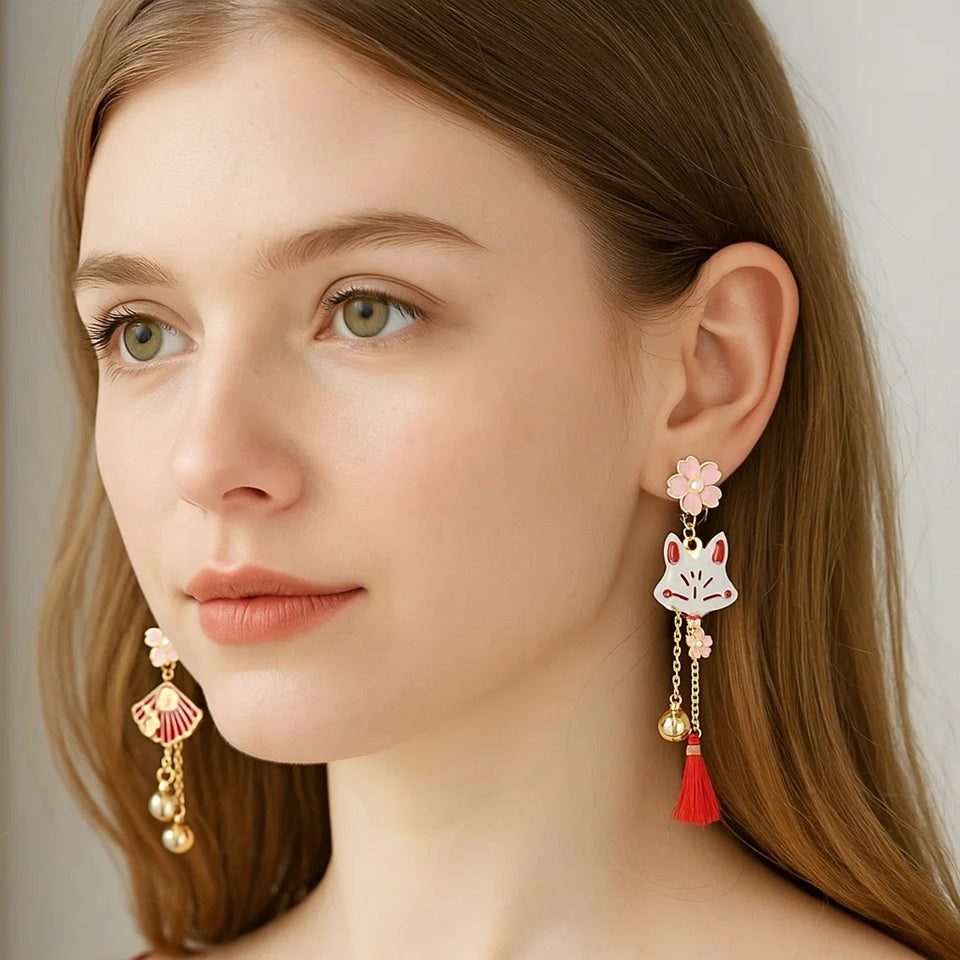 une paire de boucles d'oreilles asymétriques inspirées du folklore japonais. d'un côté un kitsune  avec un petit pompon rouge, de l'autre, un éventail. L'ensemble des couleurs rouge et blanc forment une harmonie parfaite. Des petites clochettes viennent compléter le tout.