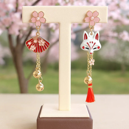 une paire de boucles d'oreilles asymétriques inspirées du folklore japonais. d'un côté un kitsune  avec un petit pompon rouge, de l'autre, un éventail. L'ensemble des couleurs rouge et blanc forment une harmonie parfaite. Des petites clochettes viennent compléter le tout.