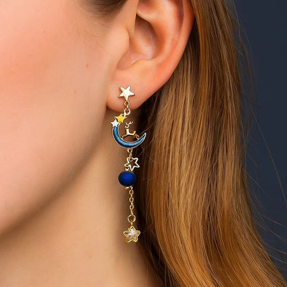 une paire de boucles d'oreilles asymétriques composée d'un côté d'un nuage et d'une perle bleue, et de l'autre, d'une lune et d'un strass en forme d'étoile