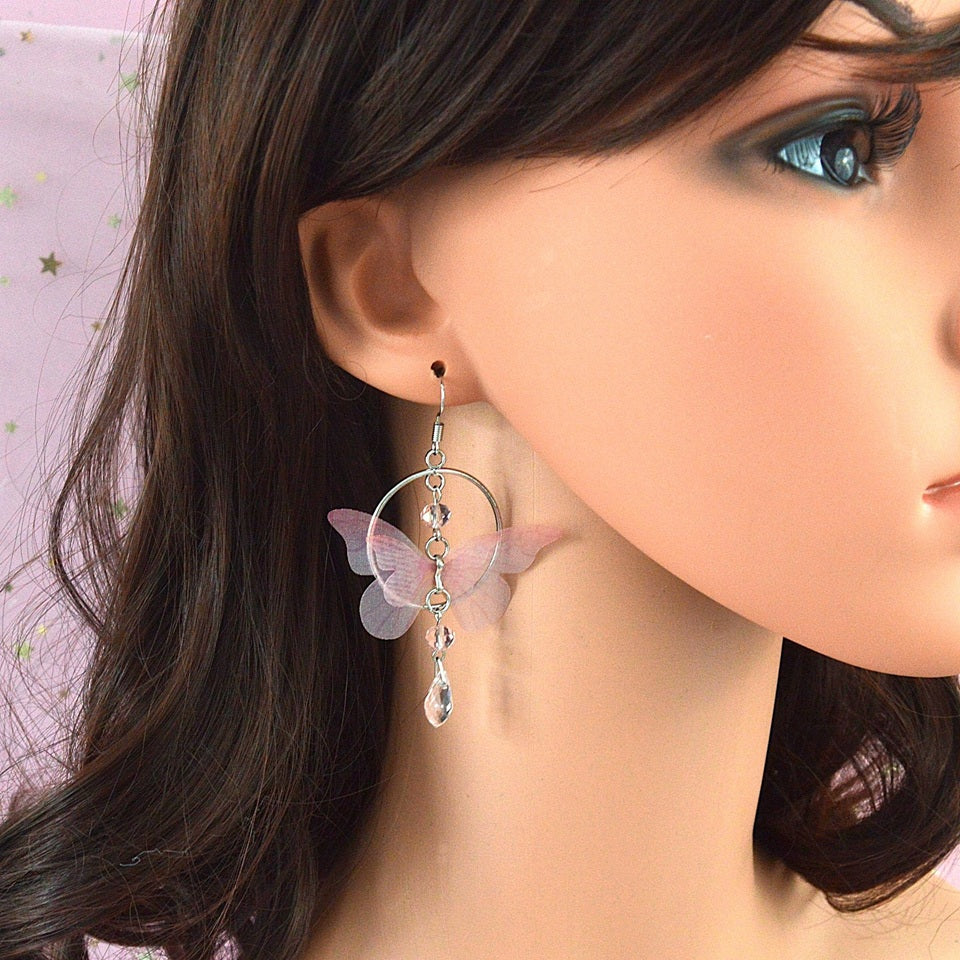 des boucles d'oreilles façon créole argenté composé d'un joli papillon en tissu rose. De jolis strass roses viennent compléter l'ensemble et ajouter une touche bohème et légère