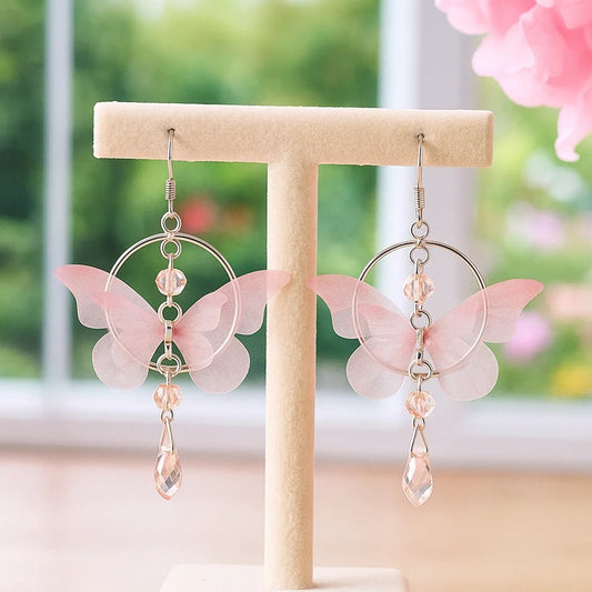 des boucles d'oreilles façon créole argenté composé d'un joli papillon en tissu rose. De jolis strass roses viennent compléter l'ensemble et ajouter une touche bohème et légère