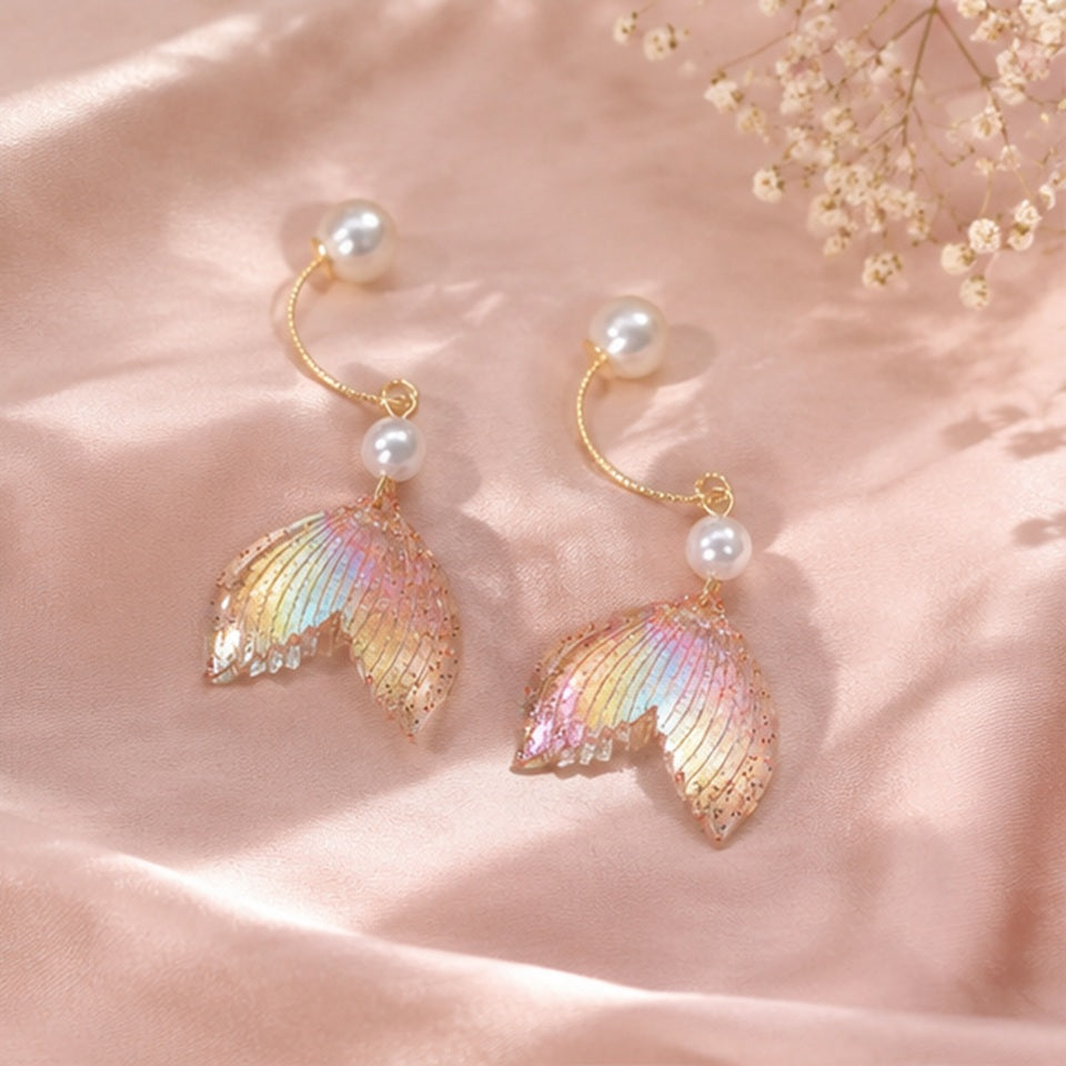 des boucles d'oreilles en forme de queues de sirènes pailletées et roses. De jolies perles blanches viennent ajouter de l'élégance à l'ensemble