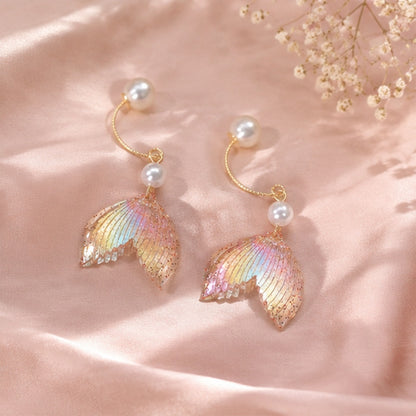 des boucles d'oreilles en forme de queues de sirènes pailletées et roses. De jolies perles blanches viennent ajouter de l'élégance à l'ensemble