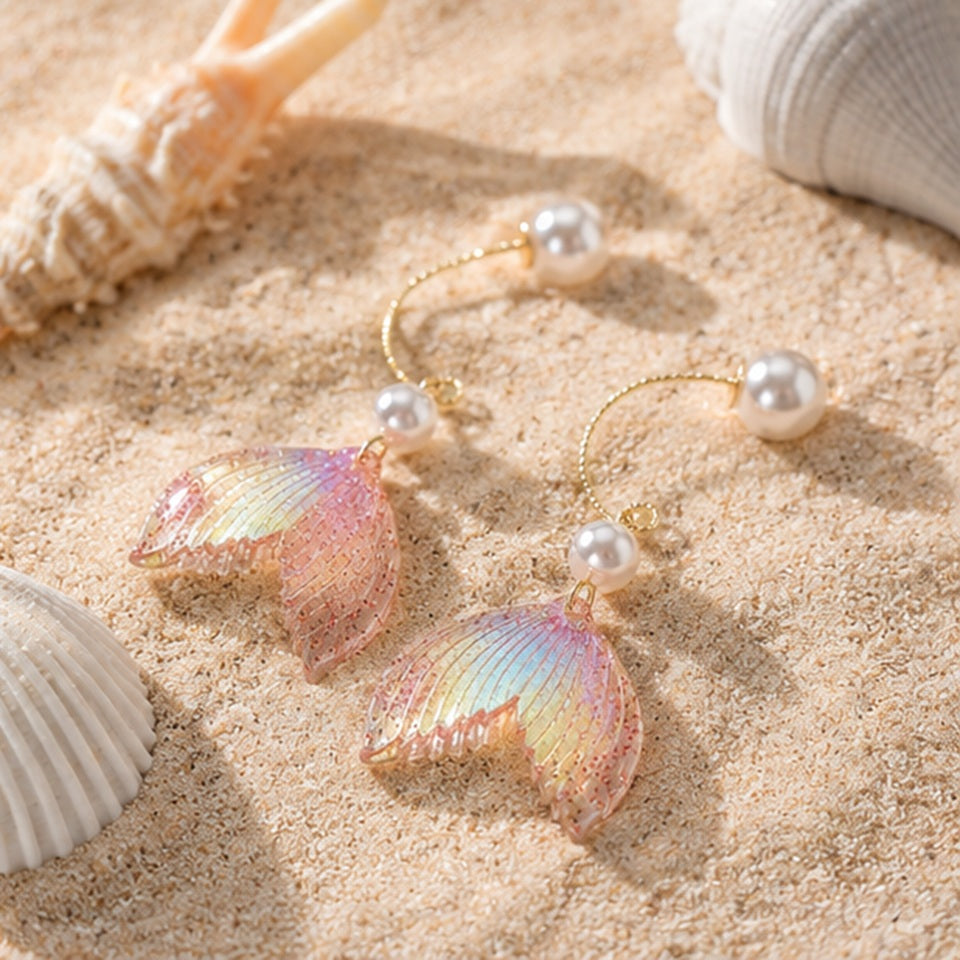 des boucles d'oreilles en forme de queues de sirènes pailletées et roses. De jolies perles blanches viennent ajouter de l'élégance à l'ensemble