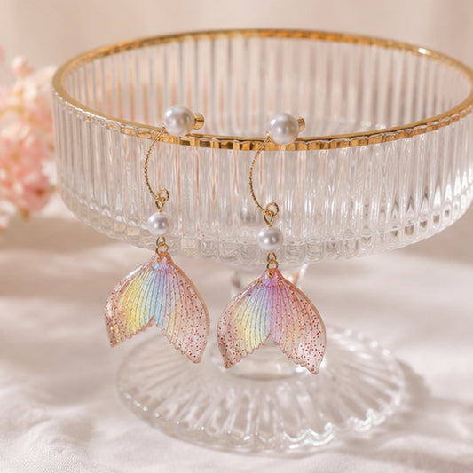 des boucles d'oreilles en forme de queues de sirènes pailletées et roses. De jolies perles blanches viennent ajouter de l'élégance à l'ensemble