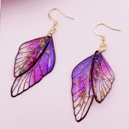 des boucles d'oreilles en forme d'ailes de fées colorées et toute pailletées. Elles semblent sortis d'un conte