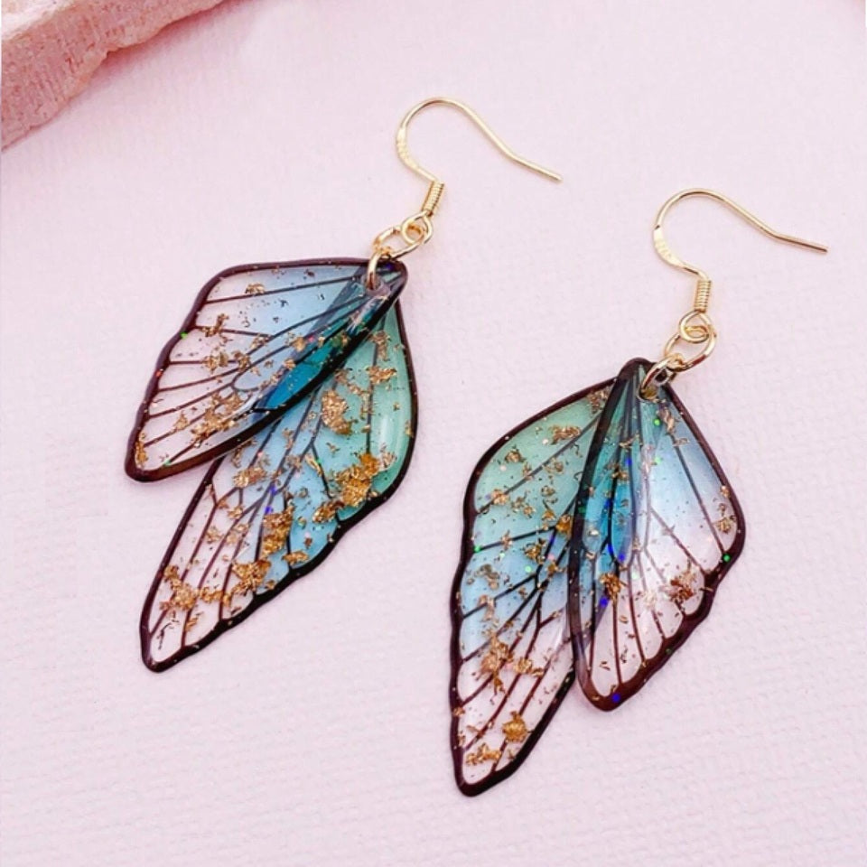 des boucles d'oreilles en forme d'ailes de fées colorées et toute pailletées. Elles semblent sortis d'un conte